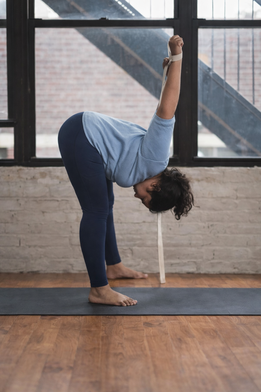 Person practicing yoga in a studio with large windows.
